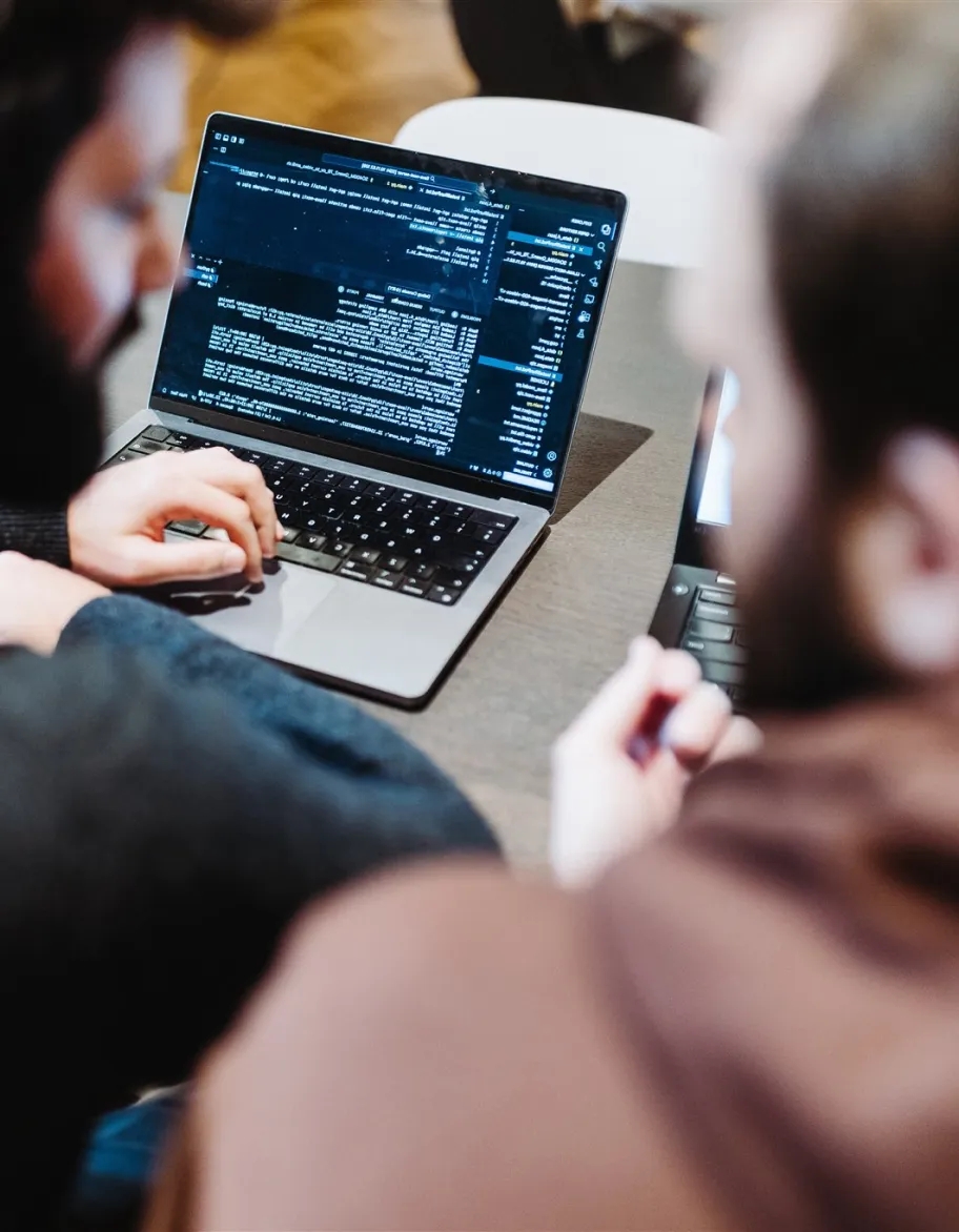 Two engineers, slightly out of focus, working on laptops.