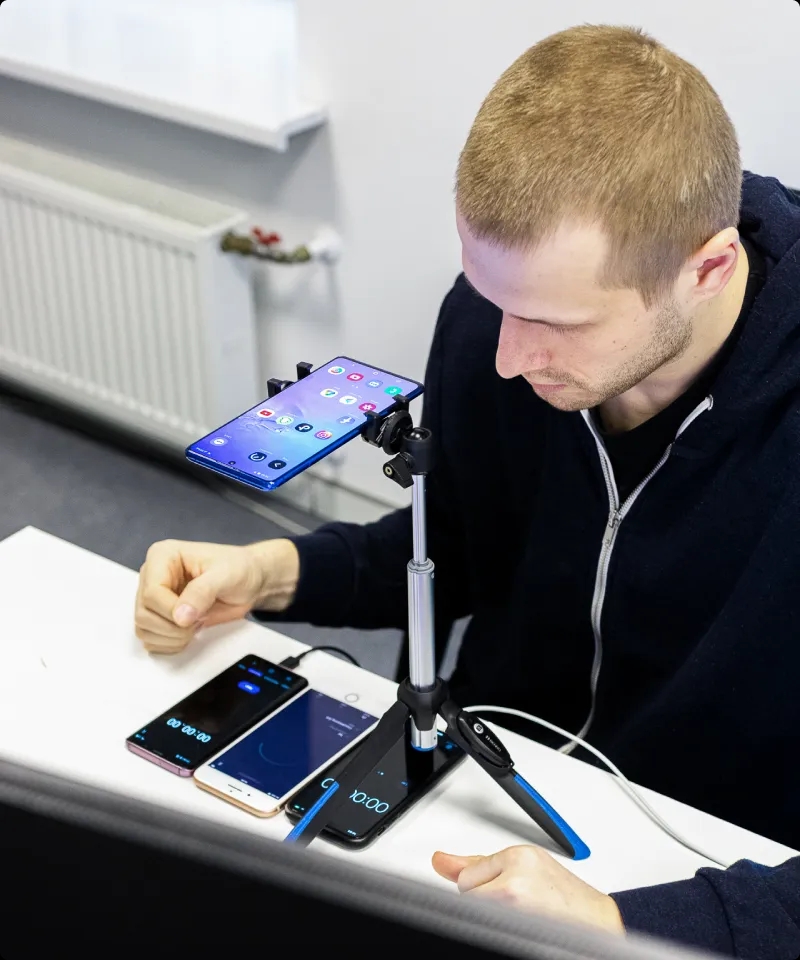 Un ingeniero de QA trabajando con 4 teléfonos móviles en el escritorio, con uno colocado en un trípode.