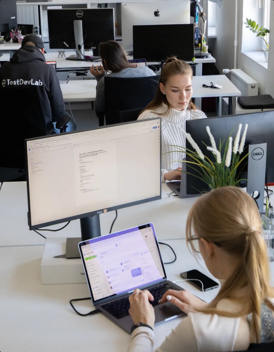 Et åbent kontorlandskab med flere personer, der sidder ved deres skriveborde og arbejder på bærbare computere.