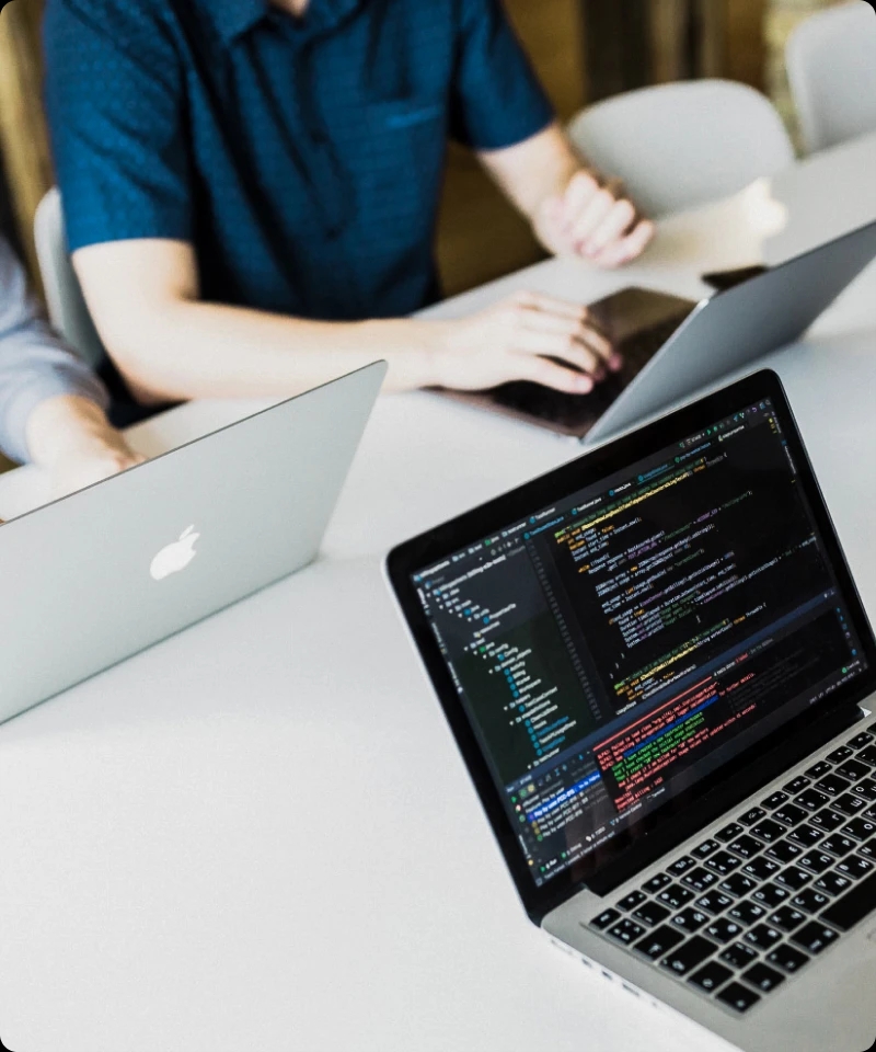 3 laptops on a table with engineers reviewing code.