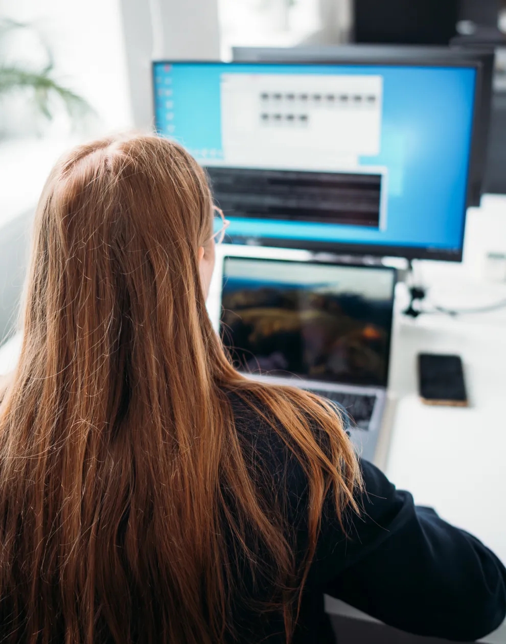 Una mujer sentada en un escritorio, trabajando en un portátil conectado a un gran monitor.