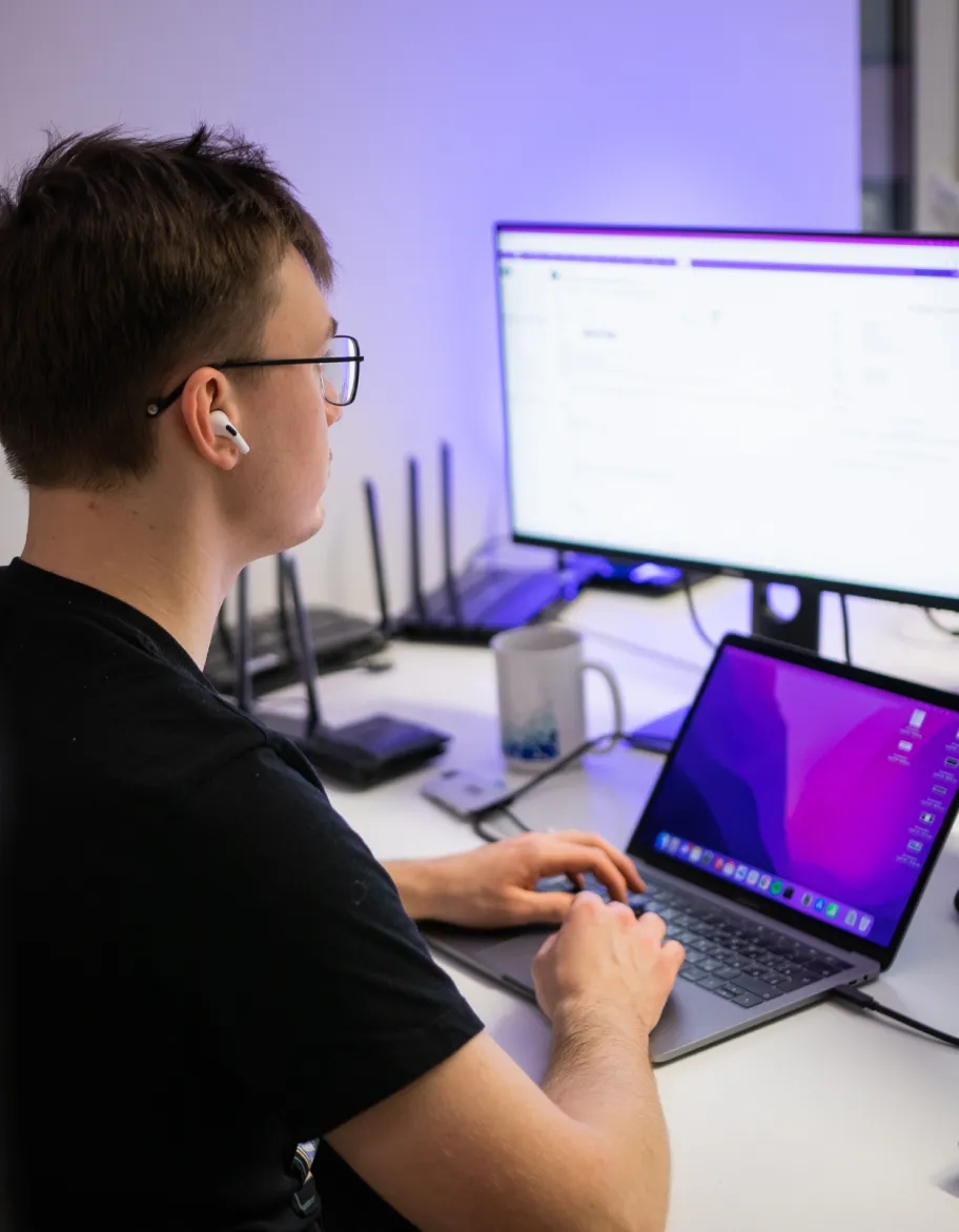 A network engineer sitting at a desk, working on a laptop while also viewing an external monitor.
