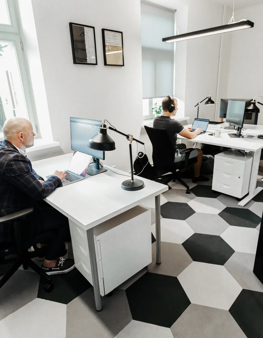 An open space with two QA engineers sitting at desks, working with their laptops.