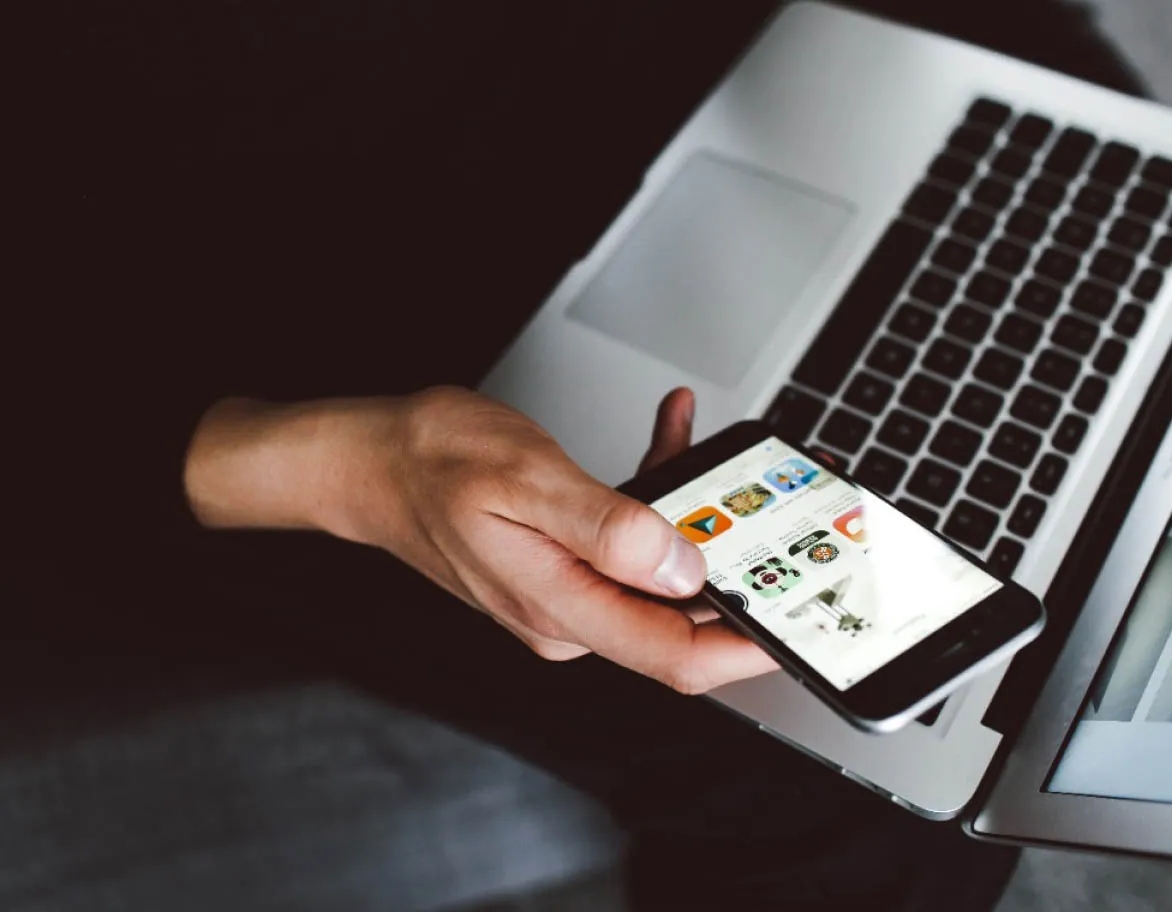 A person holding a laptop and using a mobile phone.