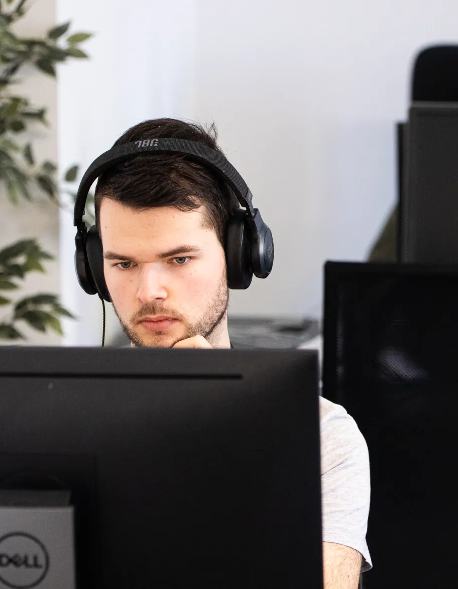 QA engineer sitting at the table, wearing headphones and looking at the monitor.