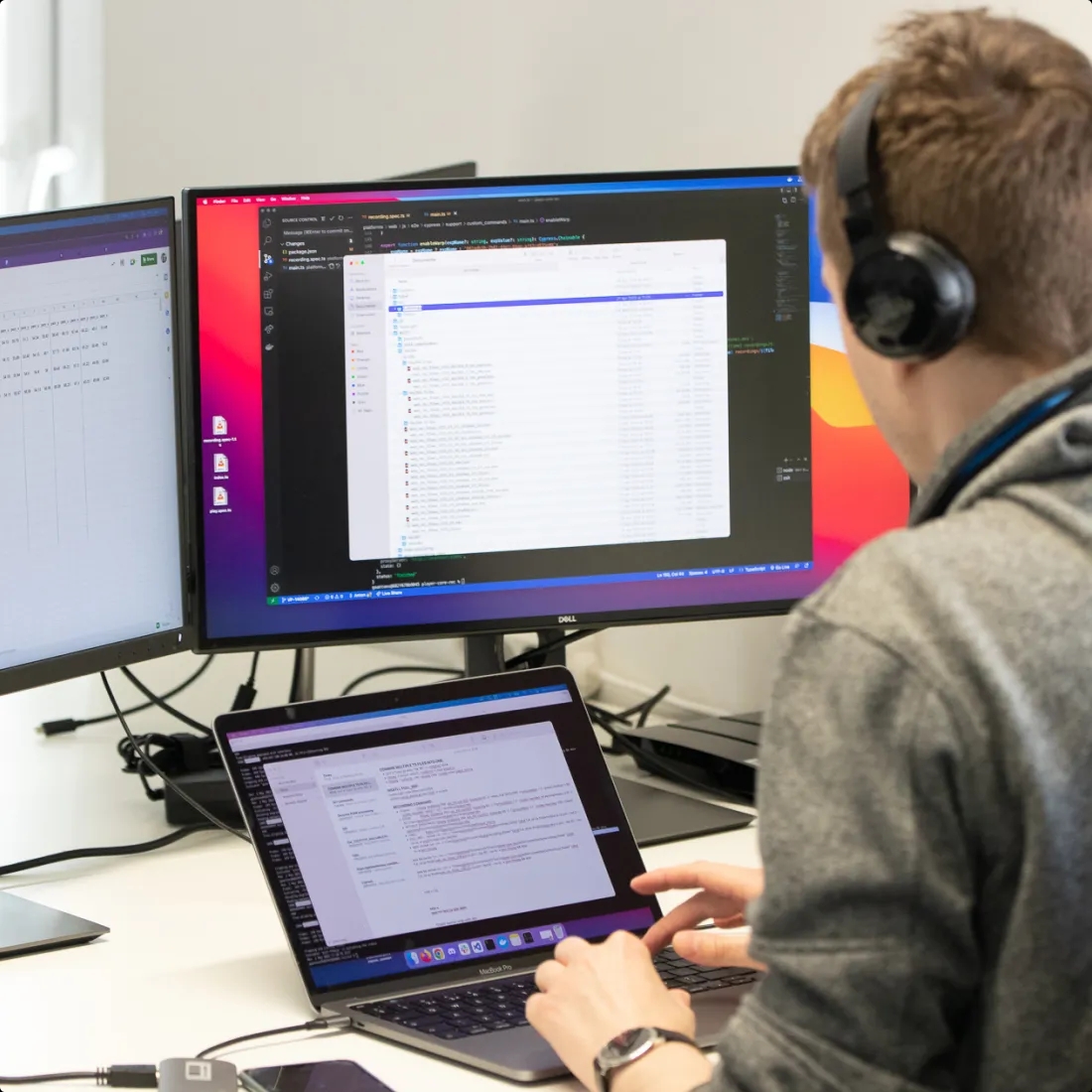 A QA engineer working with a laptop with two extra monitors hooked up to it.