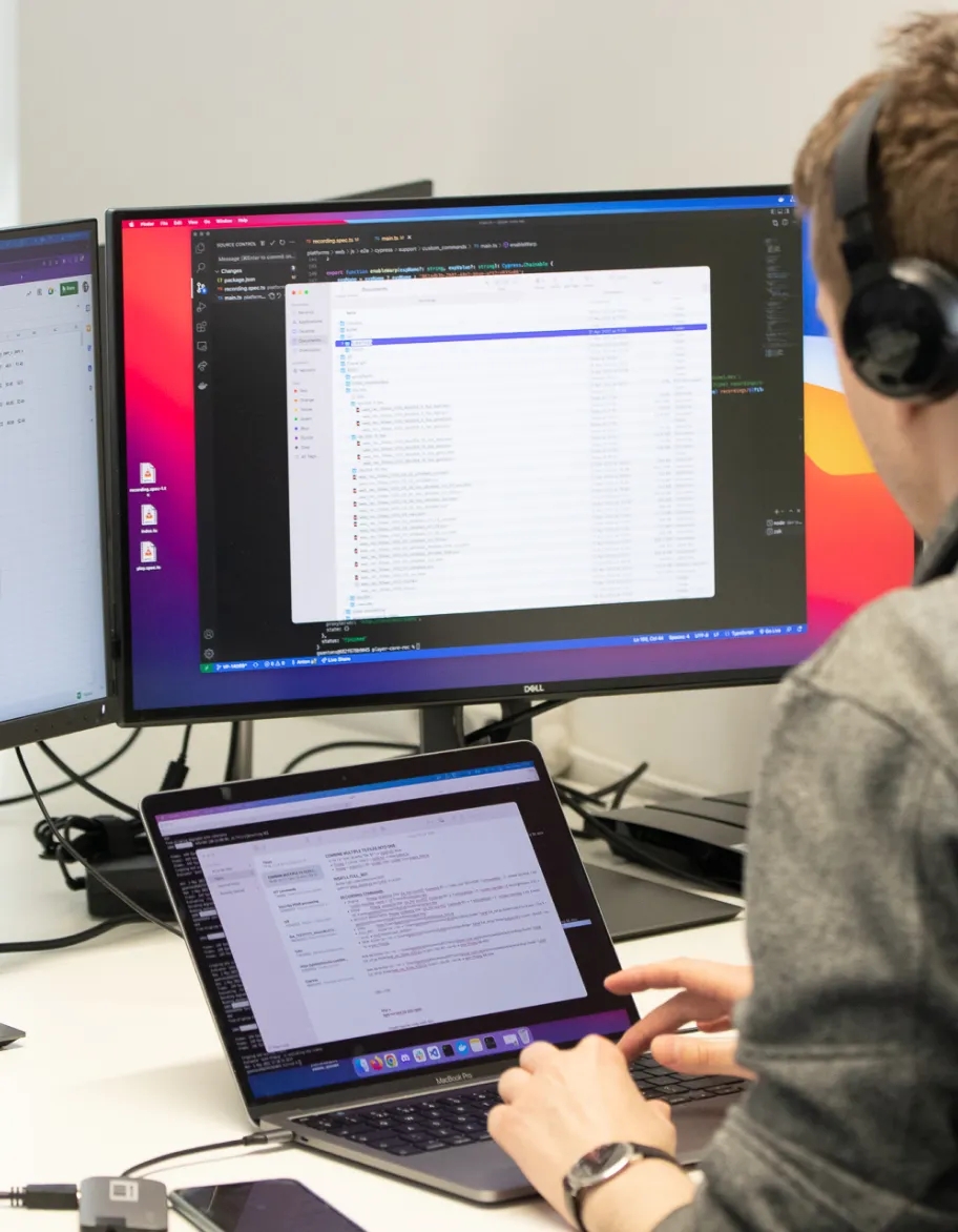 QA engineer sitting at the table with two monitors and a laptop placed on it.
