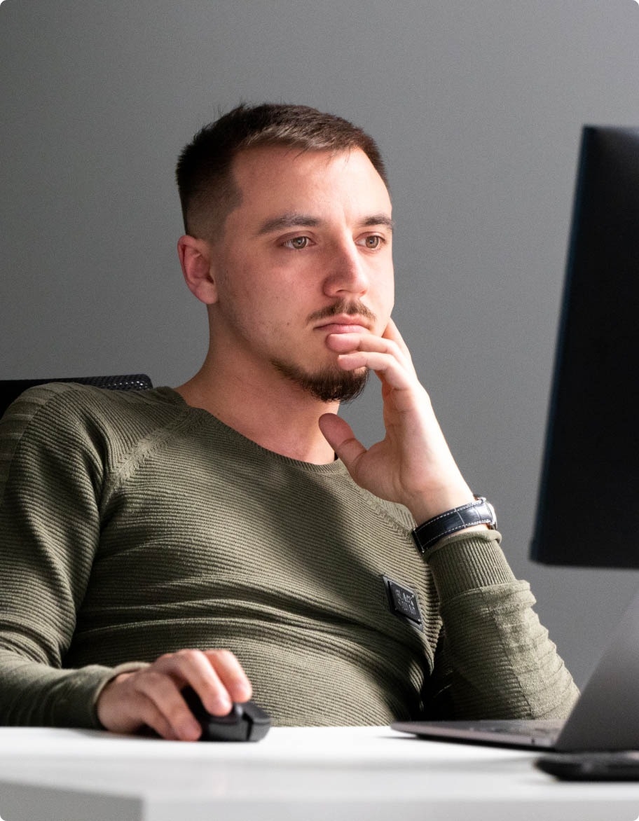 QA engineer holding a mouse and looking at a computer screen.