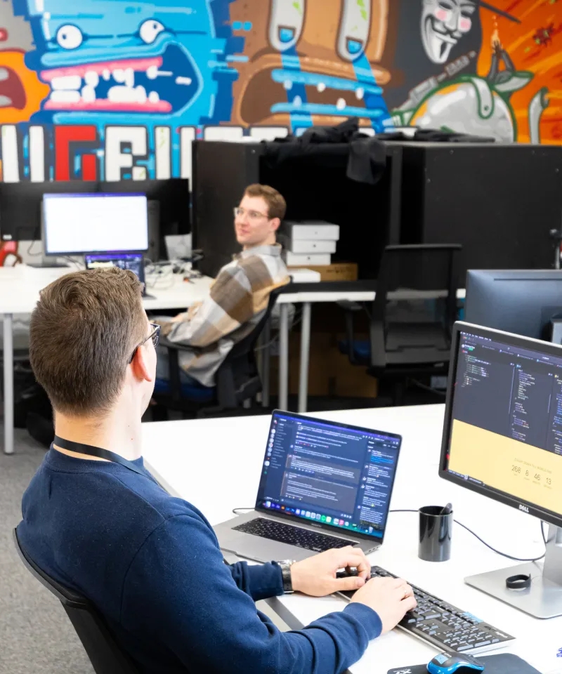 Two QA engineers in the open space, sitting at the desks and chatting.