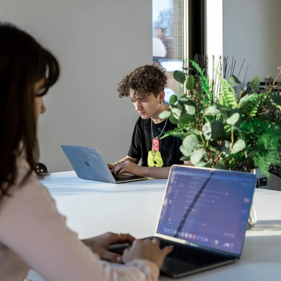 Two QA engineers sitting at a big desk and using laptops.