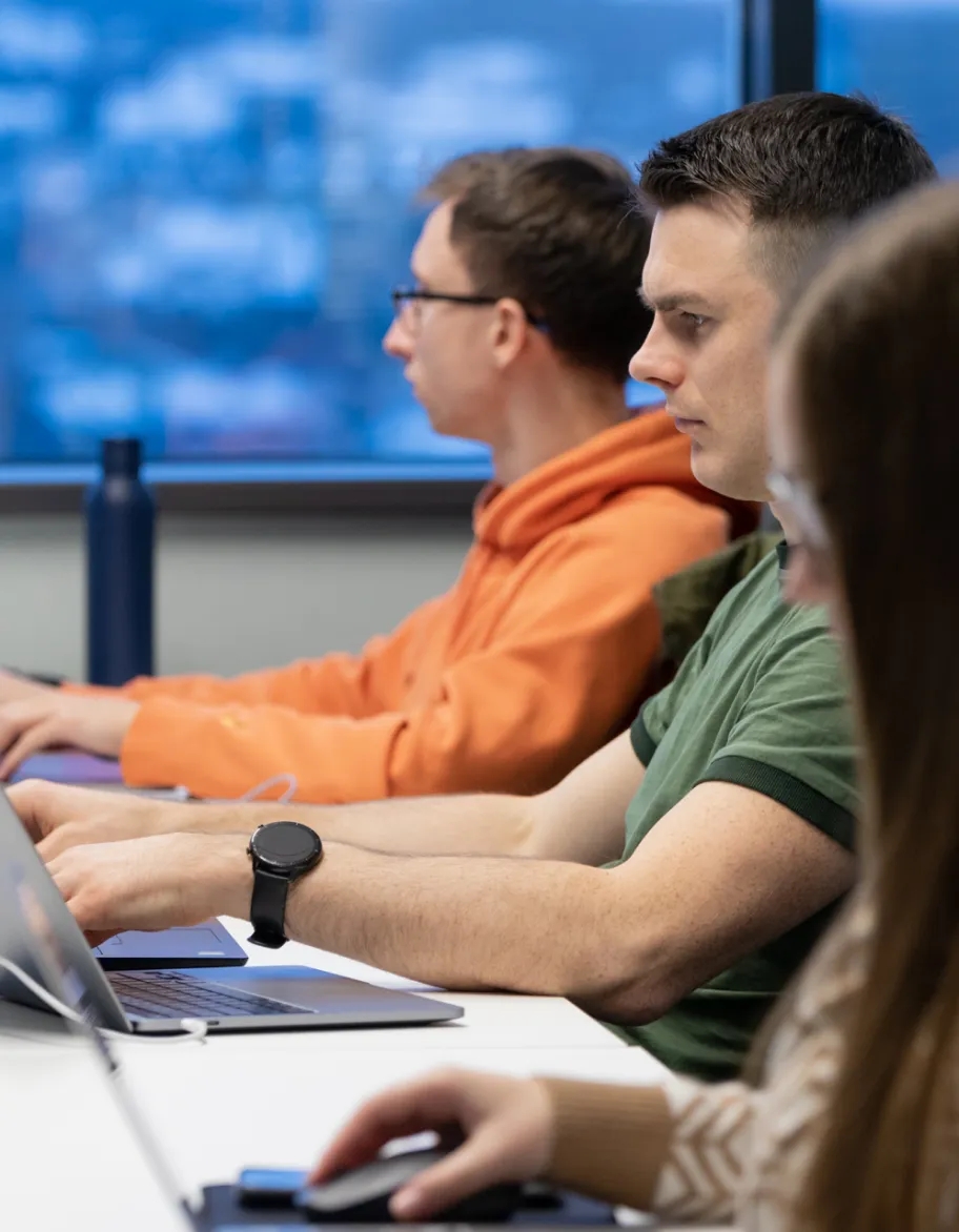 A group of QA engineers sitting at the desk with laptops on the desk, participating in a meeting.