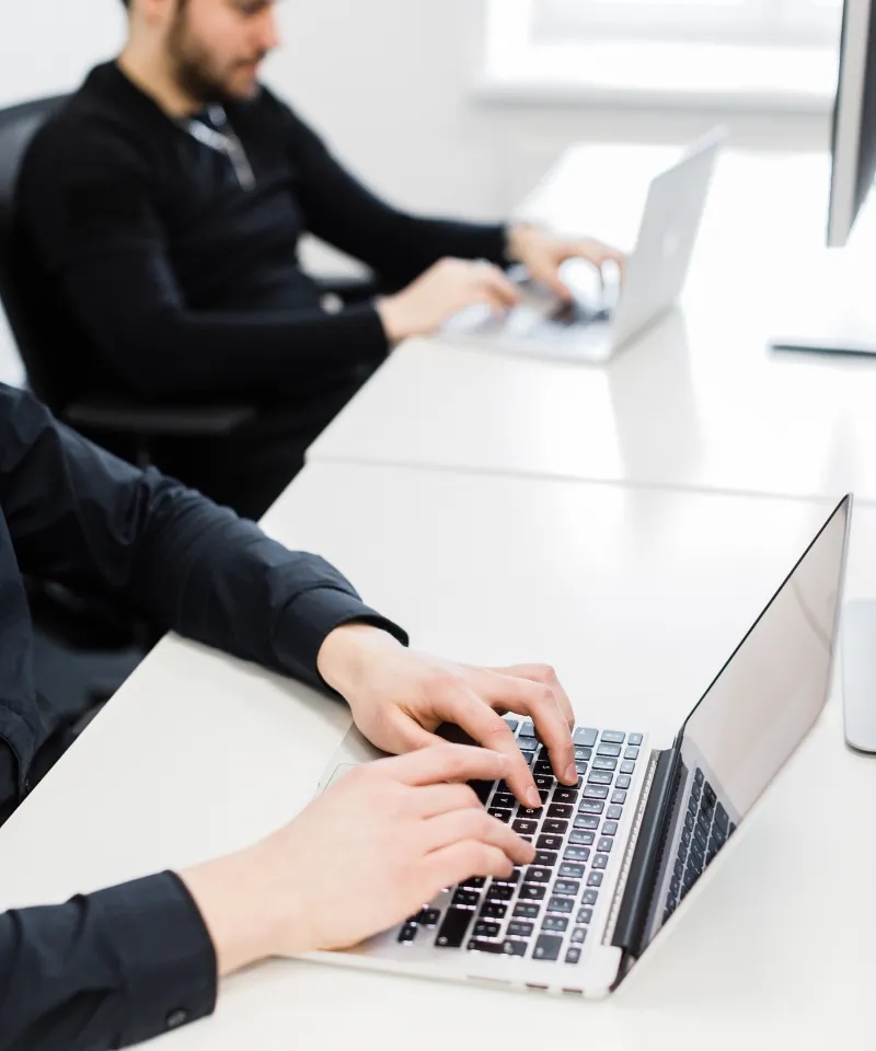 Two QA engineers sitting at the desk, using laptops.