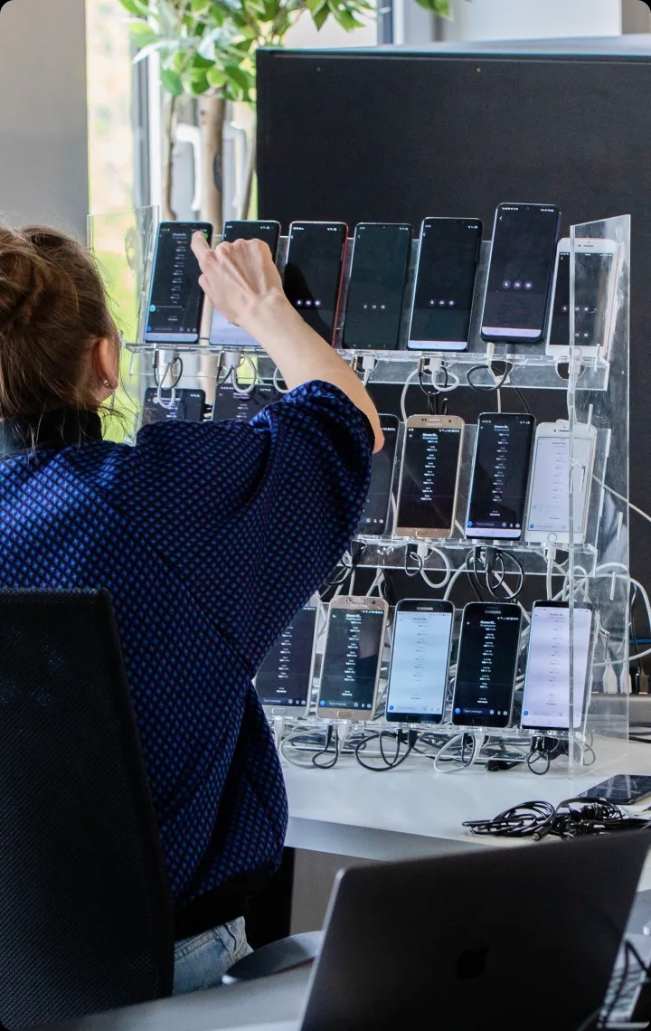 QA engineer picking a mobile phone from many test devices on a stand.