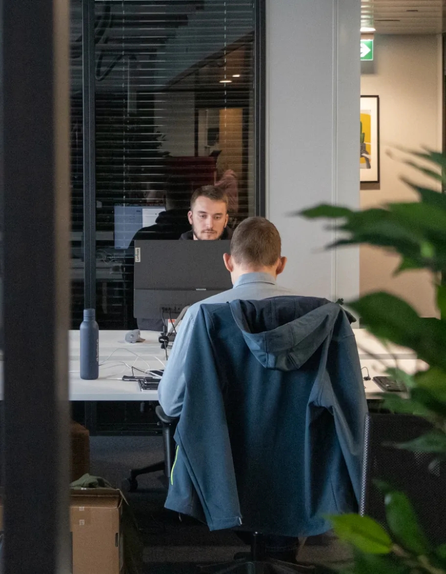 Zwei QA-Ingenieure sitzen an Schreibtischen im Büro und arbeiten mit Computern.