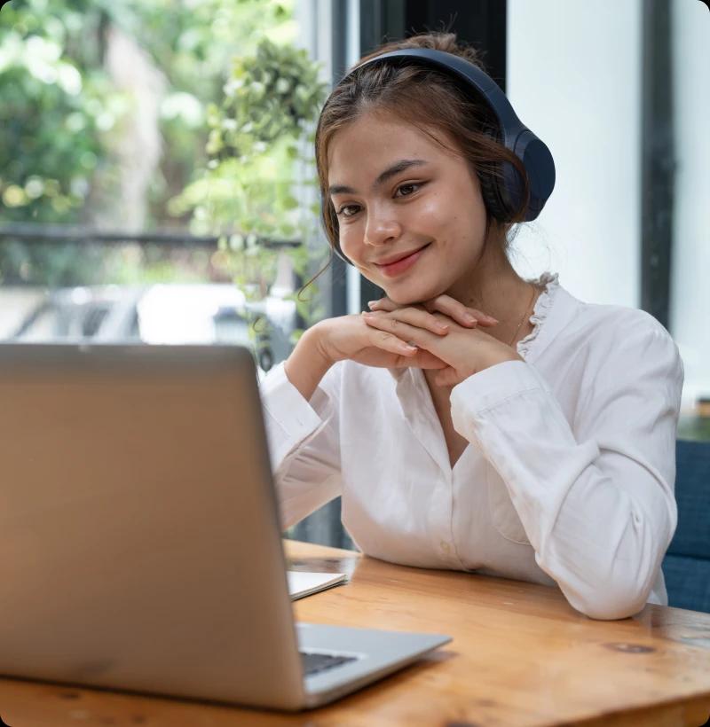An engineer sitting at her desk in front of her laptop wearing headphones and talking to a client on a remote call