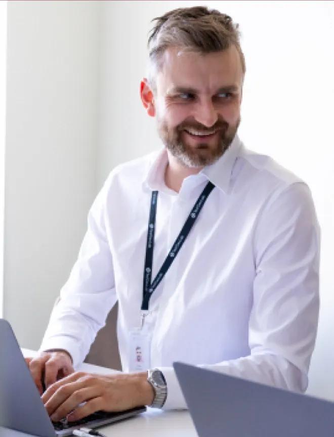 An engineer standing at the table, using a computer, and participating in a meeting.