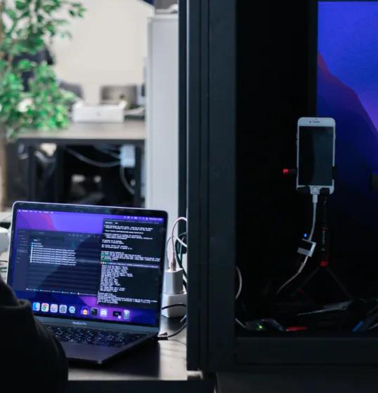 Office environment with a desk, laptop on top of it and black box with a mobile phone inside.