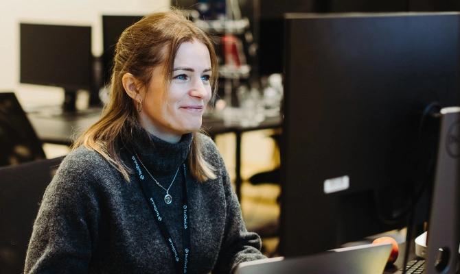 A woman looking at the external monitor placed on her desk.