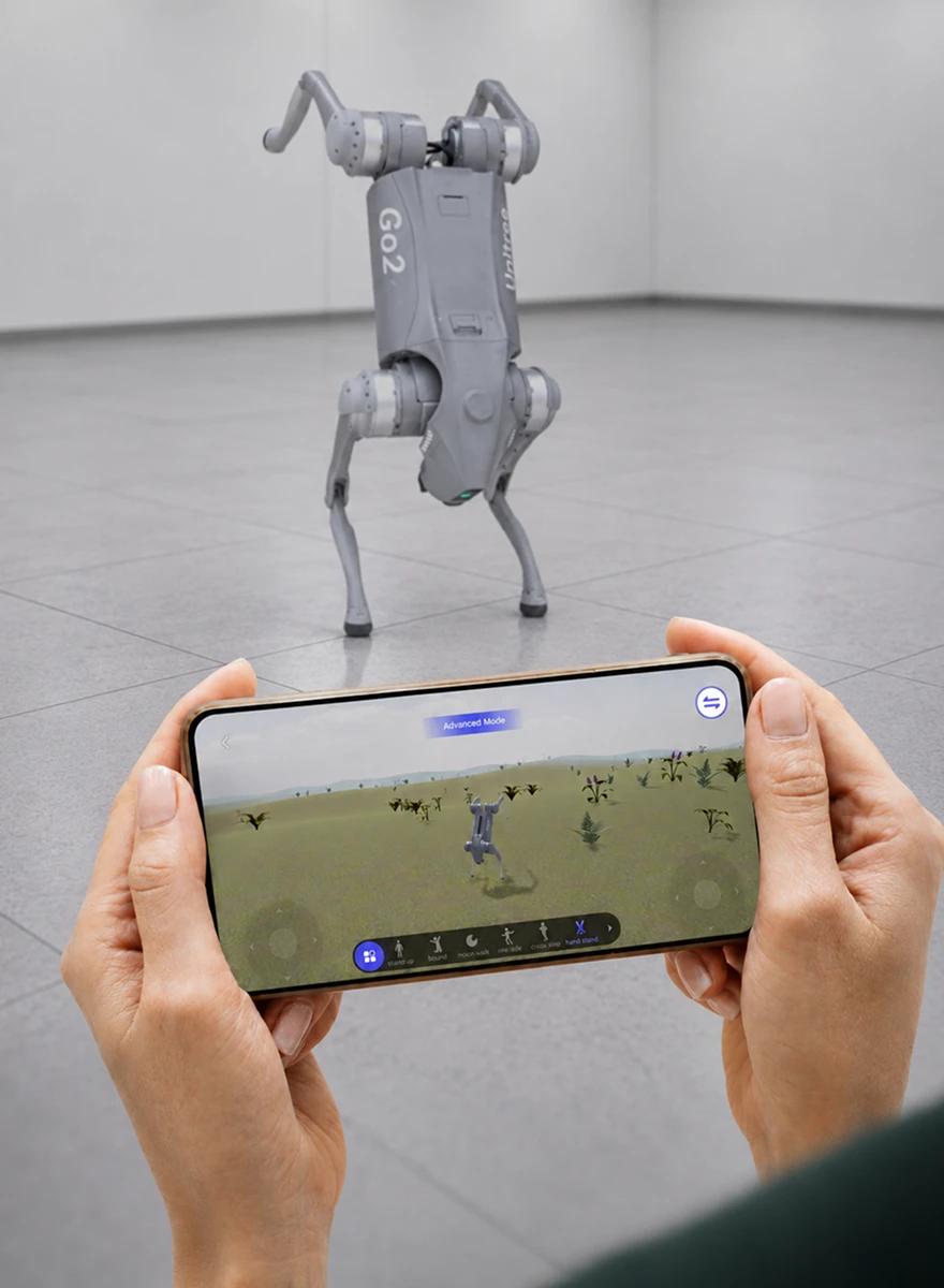 A quadruped robot standing in a test room while an engineer controls it from a handheld simulation view