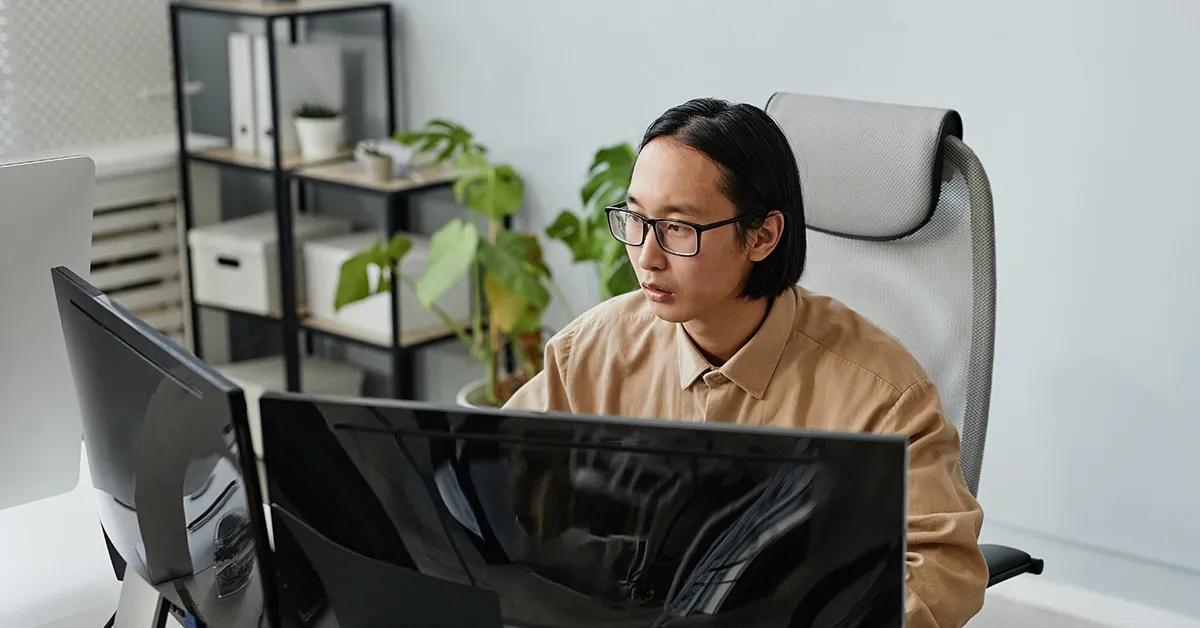 QA engineer facing and looking at two desktop computers.