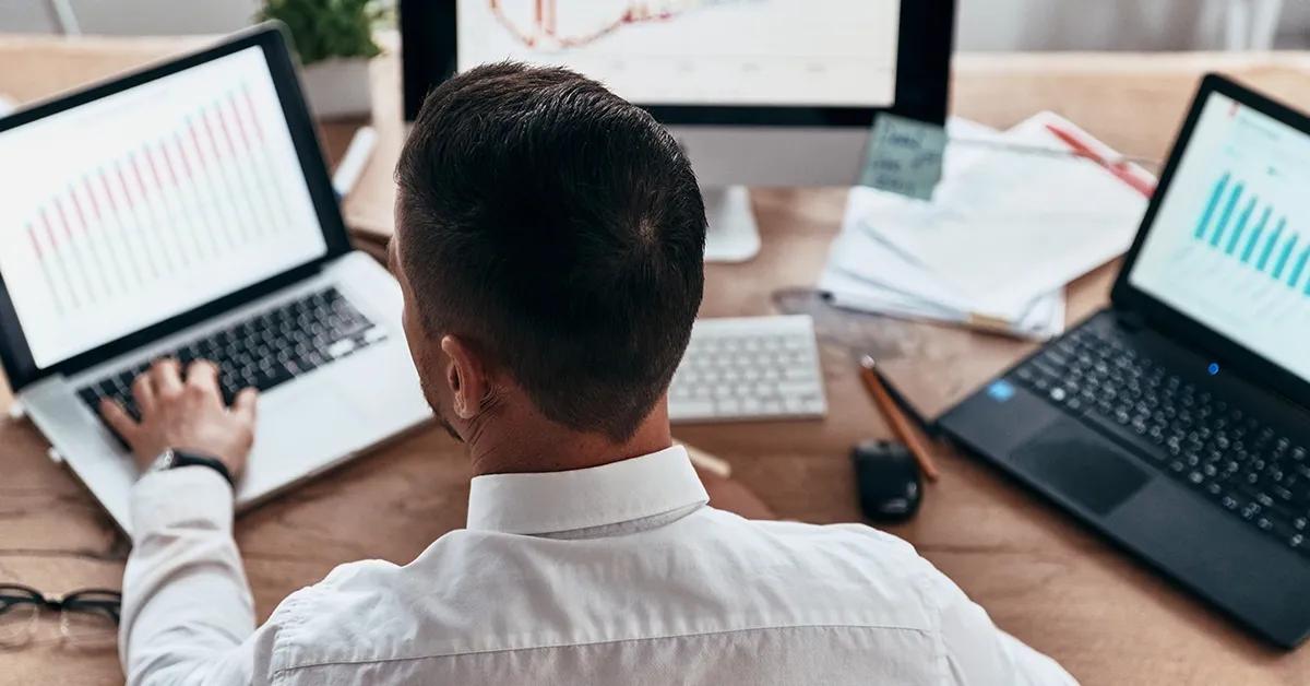 Man sitting at desk with two laptops and one desktop computer