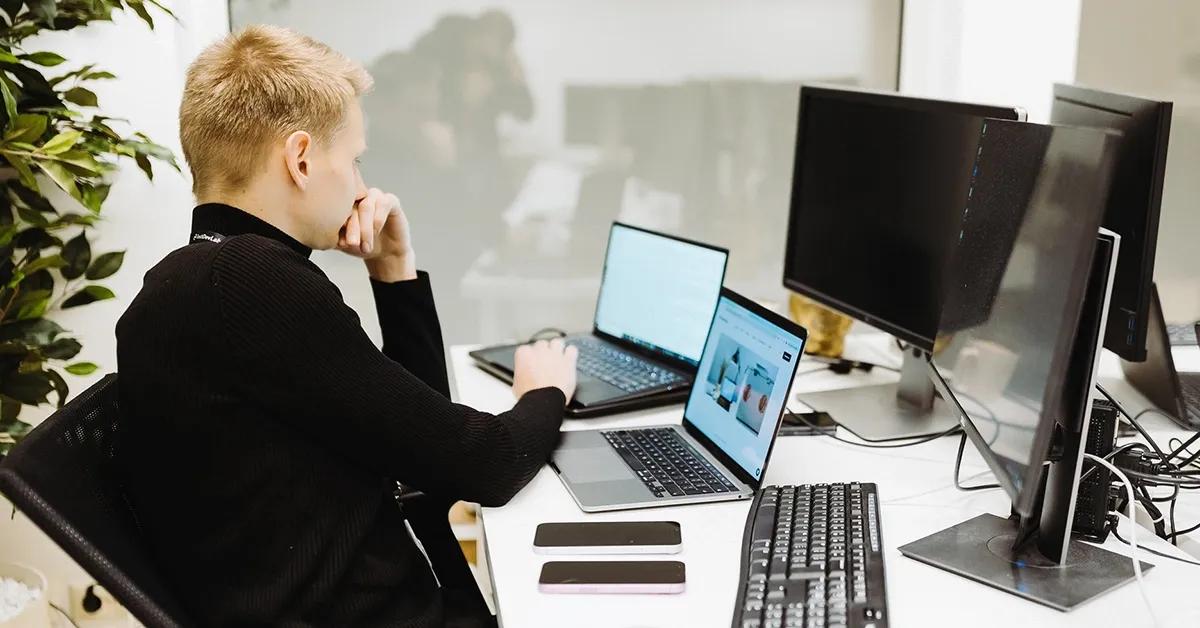 QA engineer sitting at a desk with multiple devices including laptops, smartphones and desktop computers