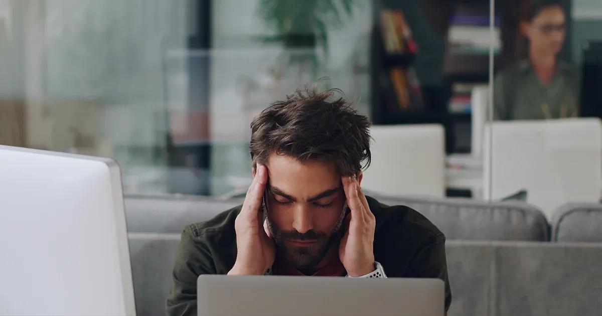 Man in an office holding his head in discomfort