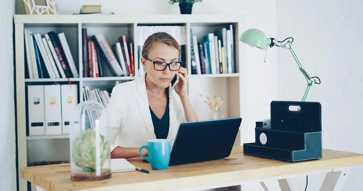 Woman talking on the phone while working on laptop at a desk