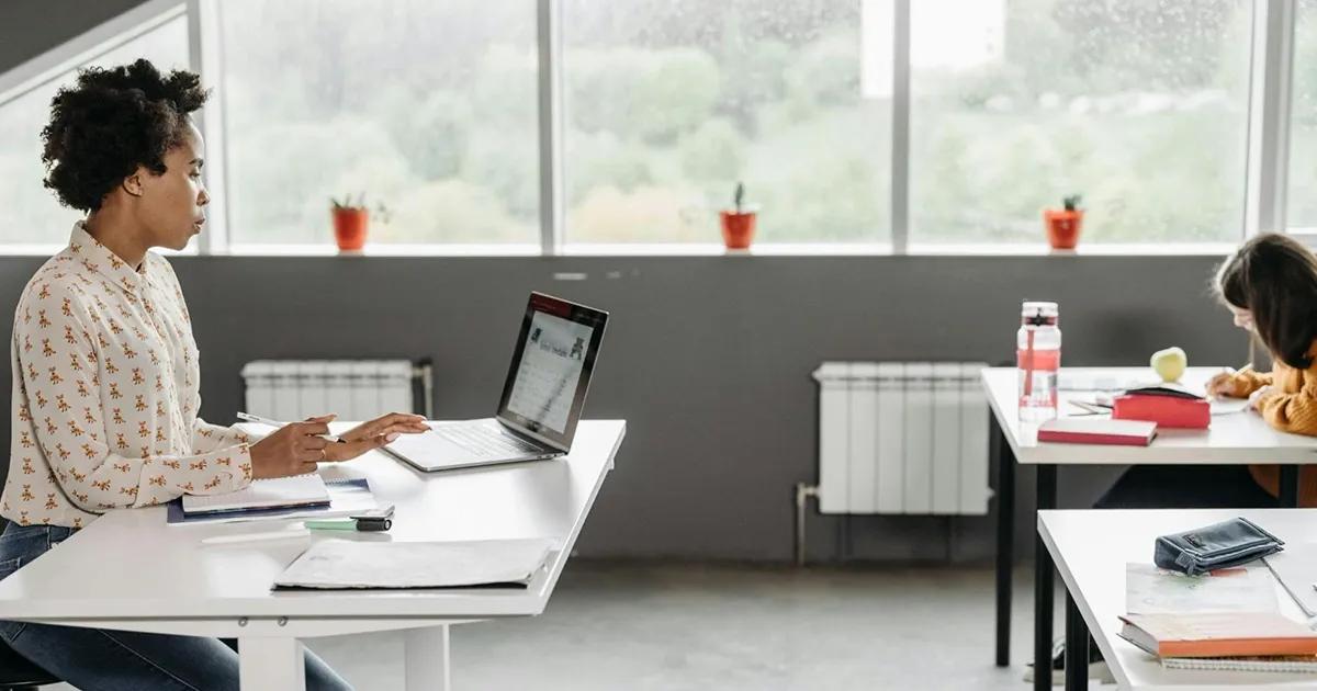 Teacher using a laptop for streaming while sitting at a desk in a classroom