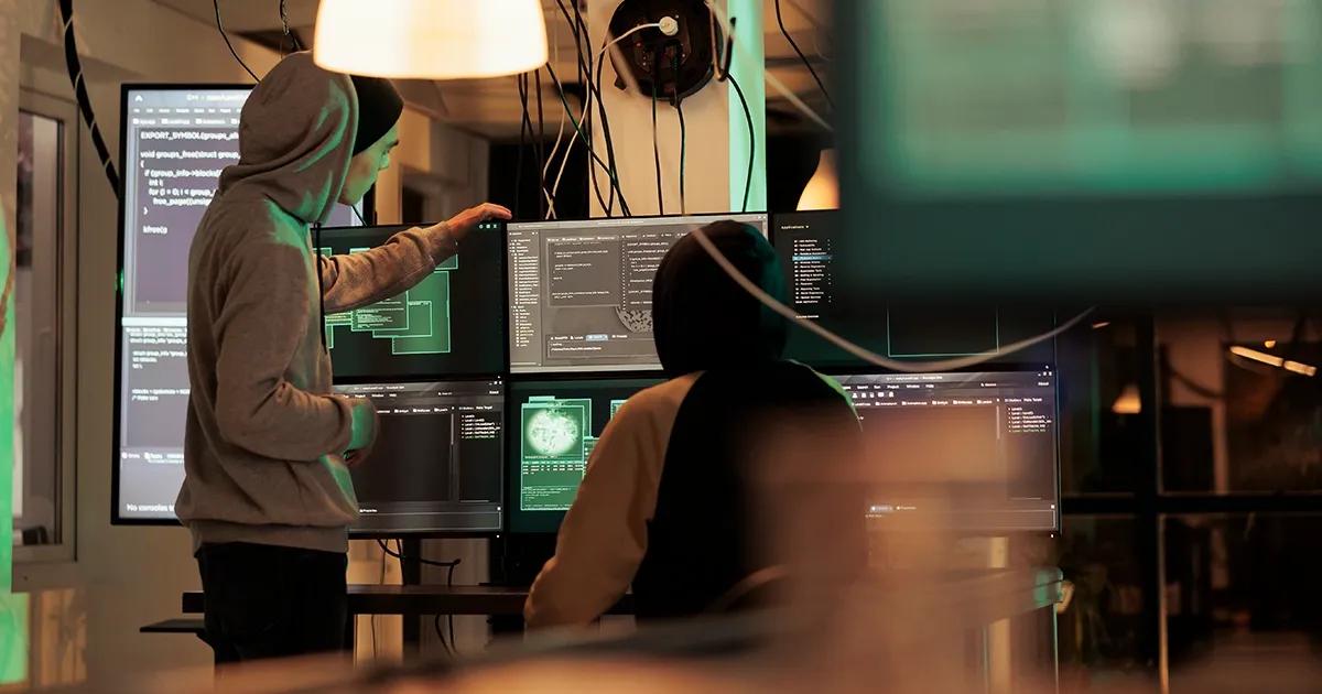 Two QA engineers in discussion while looking at multiple computer screens