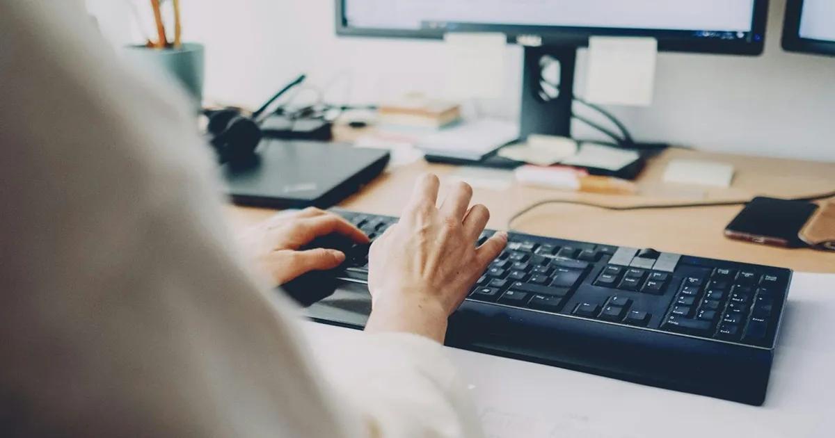 Person typing on keyboard at a cluttered desk