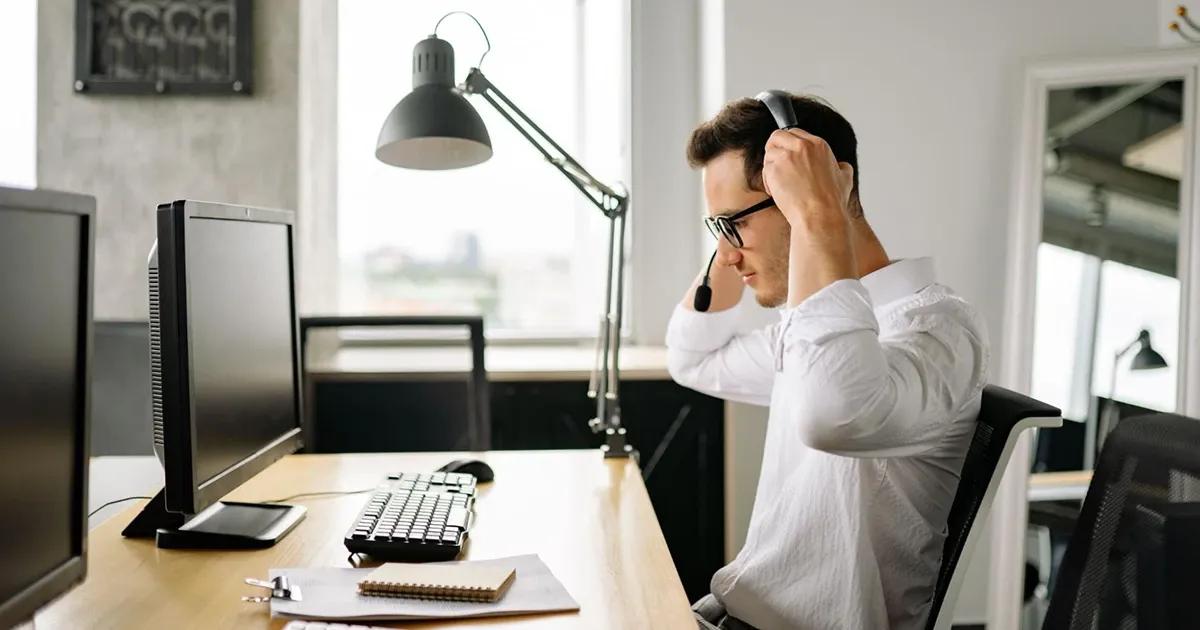 QA engineer putting on headphones while sitting at a desk with a desktop computer