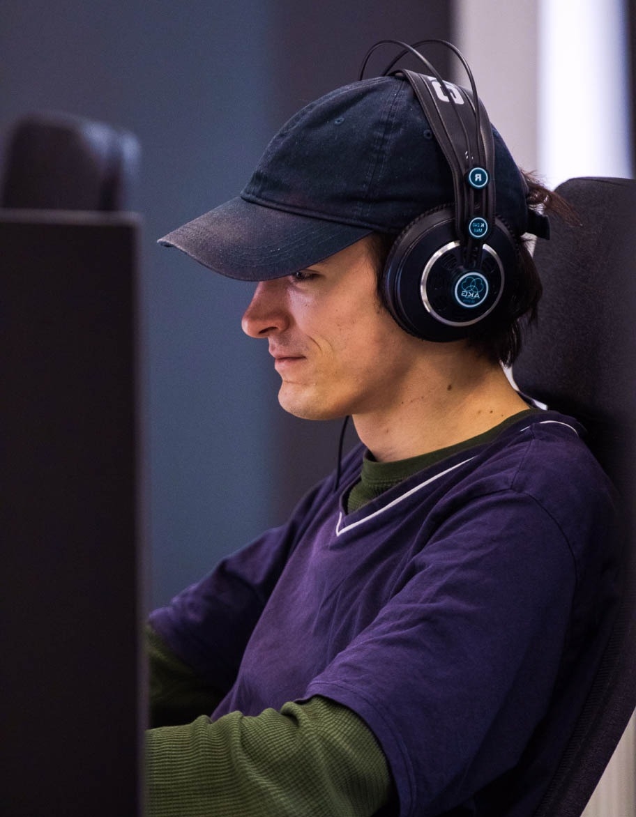 Ingeniero de control de calidad con gorra y auriculares sentado en el escritorio y trabajando en un proyecto de pruebas de videojuegos.