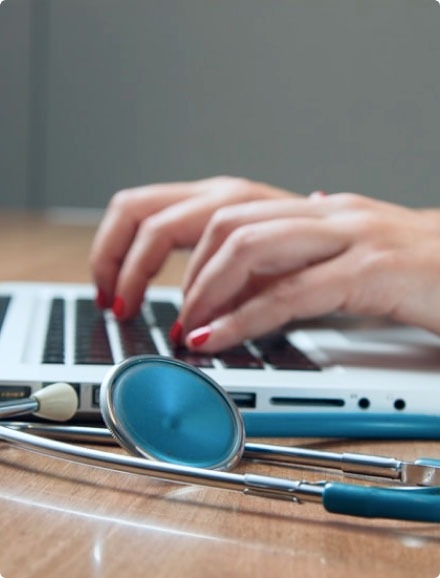 A close-up of a stethoscope and a person typing on a laptop.