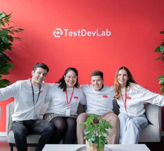 Quatre ingénieurs QA portant des sweat-shirts blancs avec le logo de TestDevLab prennent une photo de groupe.