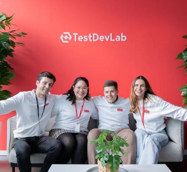 Four QA engineers wearing white hoodies with the TestDevLab logo taking a group photo.