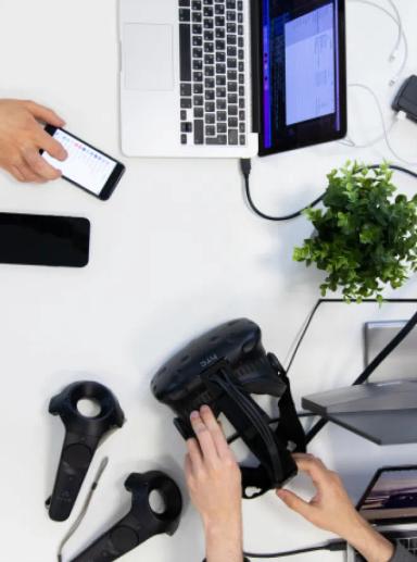 Billedet af bordpladen viser VR-headset og mobiltelefoner placeret på et hvidt skrivebord.