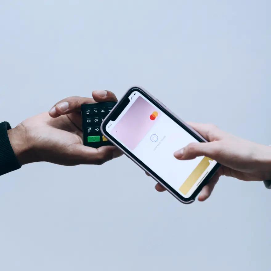 One hand holding a card reader while another taps a phone against it to pay