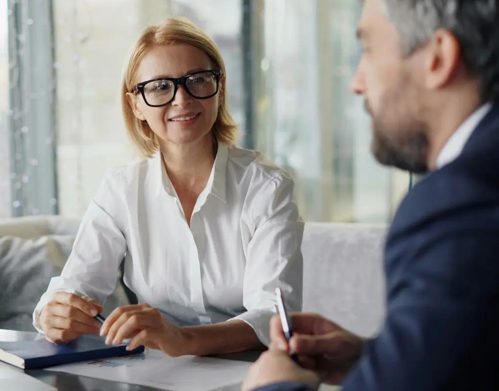 Two people in business dress talking across a table while one of them takes notes