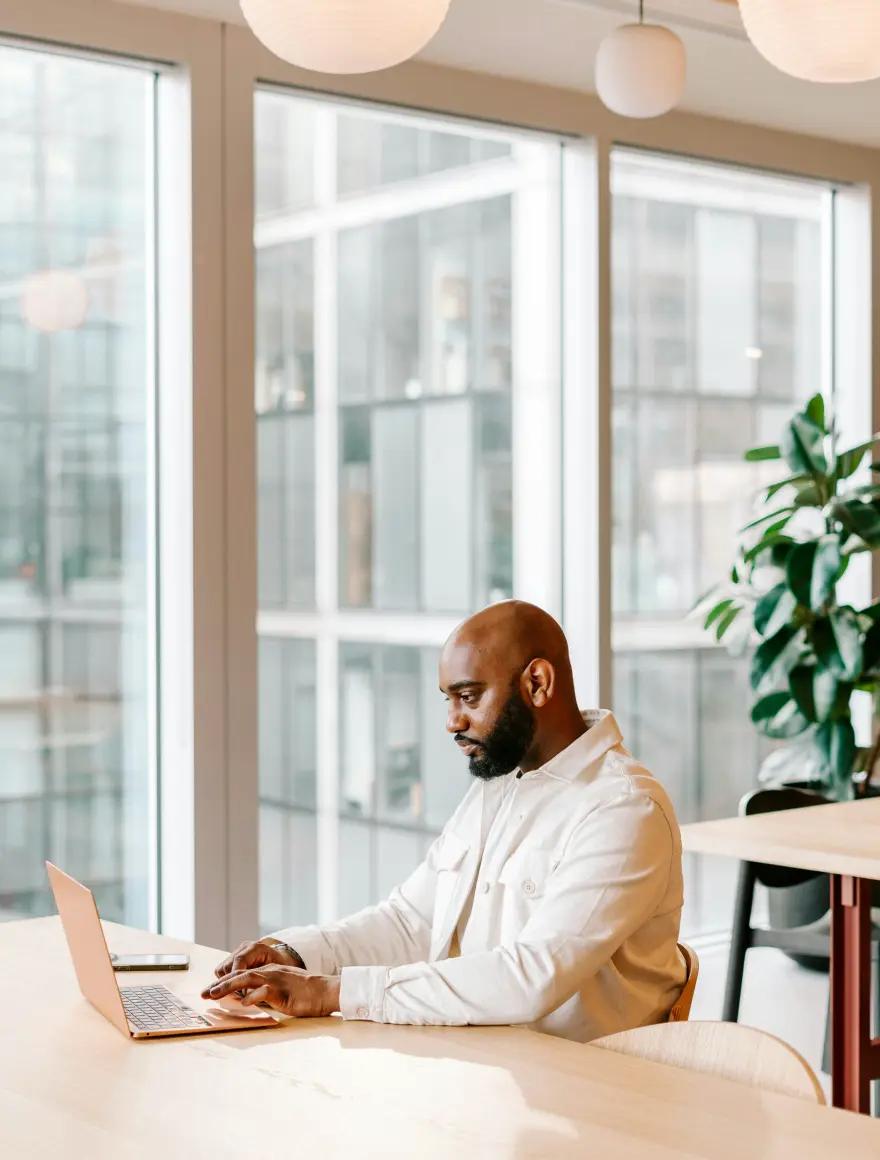 A software professional working on a laptop at an office desk by a window