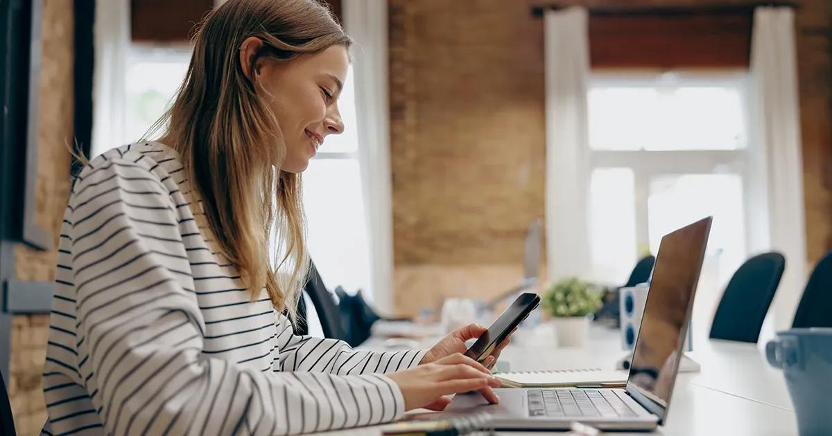Woman using a laptop and holding a phone