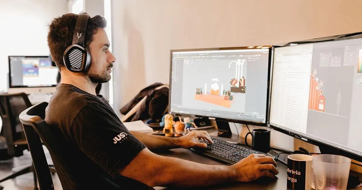 QA engineer wearing headphones and working on desktop computer with two screens