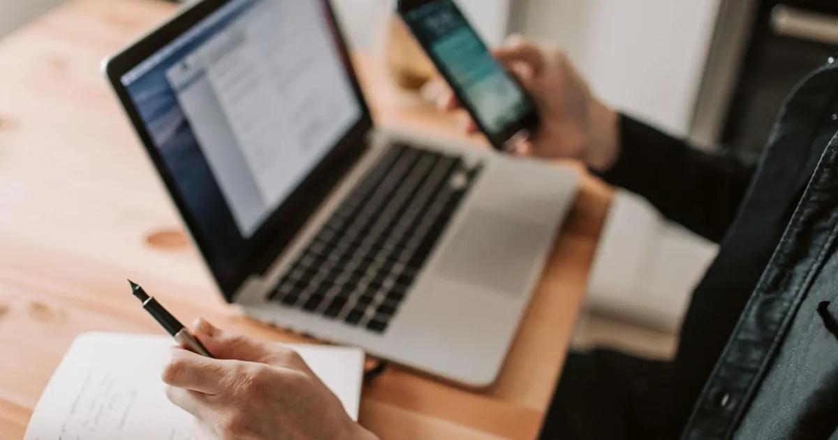 Person on a mobile phone and laptop, while holding a pen